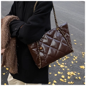 Close-up of a large brown quilted shoulder bag with gold chain strap and metal charm