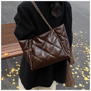 Close-up of dark brown quilted tote bag with golden chain strap on autumn street