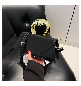 Detail of structured black leather handbag featuring a sculpted gold-tone metal top handle