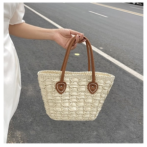Detail of woven straw tote bag with brown leather handles and textured diamond pattern