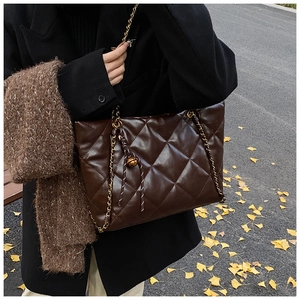 Detail of dark brown quilted tote bag with gold chain and bell charm on autumn leaves