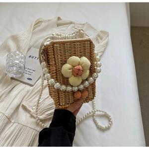 Detail of handmade woven straw bag with fabric flower, pompom, and pearl chain strap