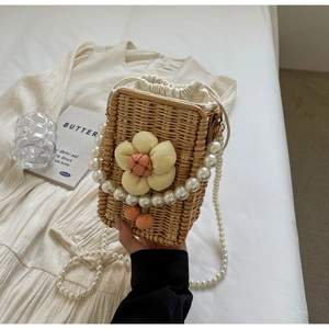 Detail of handmade woven straw bucket bag with floral decor and elegant pearl straps