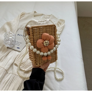 Detail of hand-woven rattan mini bag featuring pink floral decor and pearl strap