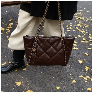 Detail shot of a dark brown quilted tote bag with golden chain strap on autumn leaves