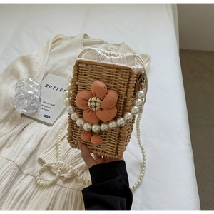 Detail of handmade straw bucket bag featuring pink fabric flowers and pearl handle strap