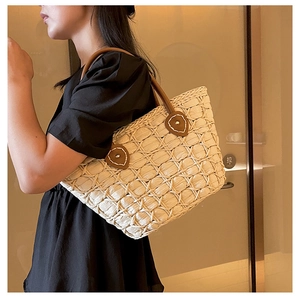 Detailed close-up of woven straw texture and premium brown leather handle on tote bag