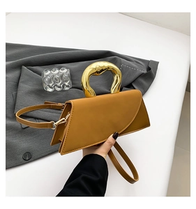 Detail of caramel brown geometric handbag with a polished gold ring handle and leather texture