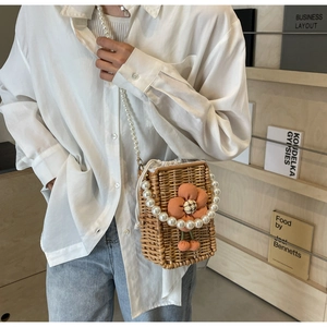 Detail of hand-woven straw bucket bag with floral accents and white pearl beaded strap
