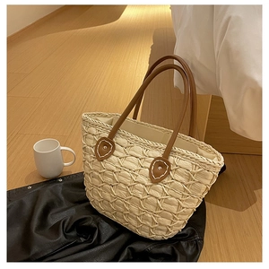 Detailed close-up of woven texture and brown leather handles on a large straw beach tote bag