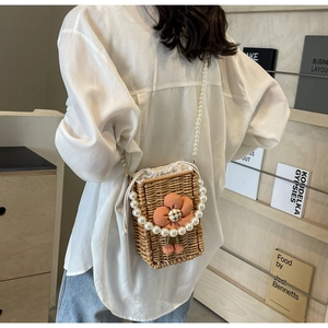 Detail of hand-woven straw crossbody bag with orange flower and pearl shoulder strap