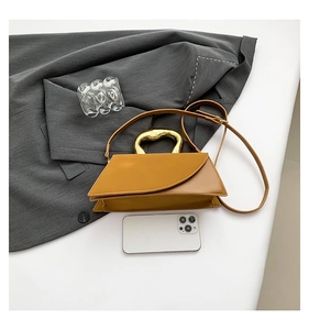 Detail of a ginger leather handbag with wave metal handle and smartphone for size scale