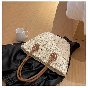 Detail of woven straw tote bag featuring brown leather handles and natural textured weave