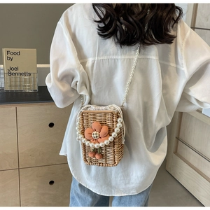 Detail of hand-woven straw bag featuring orange fabric flowers and pearl bead strap