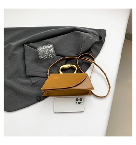 Brown leather handbag with gold metal handle and shoulder strap next to a mobile phone