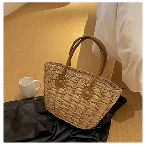 Close-up of textured woven straw bag featuring brown leather handles and metal rivets