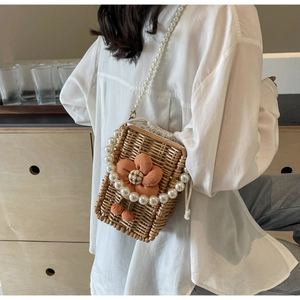 Detail of woven straw crossbody bag with orange fabric flower and pearl chain straps