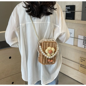 Detail of handmade woven straw bucket bag with pearl chain strap and floral decor