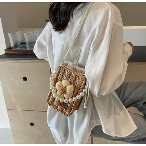 Detail of hand-woven straw bag with floral accents and a premium pearl shoulder strap
