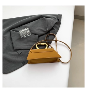 Detail of yellow trapezoid bag featuring unique gold heart-shaped metal handle and strap