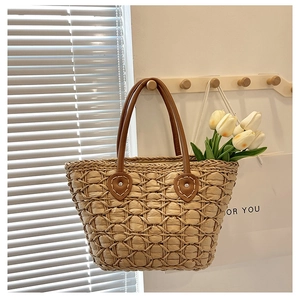 Detail of woven straw tote bag featuring brown leather straps and heart-shaped stitching