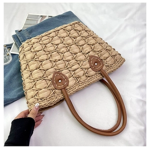 Detailed close-up of handmade straw tote bag with brown leather handles and leaf-shaped patches