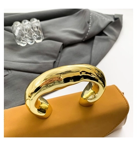 Detailed close-up of a mustard leather square bag with liquid-style gold metal handle