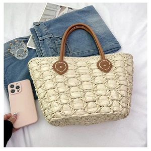 Close-up of beige woven straw beach tote with premium brown leather handles and heart detail