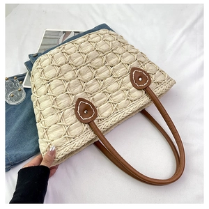 Detailed view of beige straw tote bag featuring diamond weave texture and brown leather handles