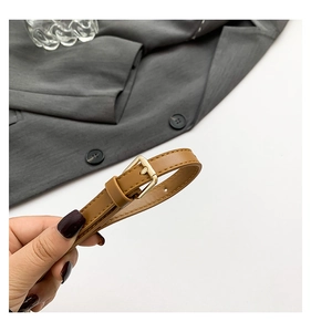 Detail of tan leather waist belt with gold pin buckle and tonal stitching accents