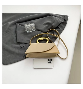 Detail view of beige square handbag with gold metal handle and shoulder strap on a blazer