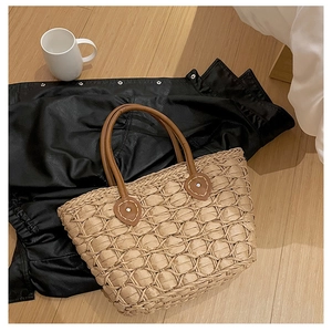 Detail of straw tote bag showing circular woven texture and leather handle with stitching