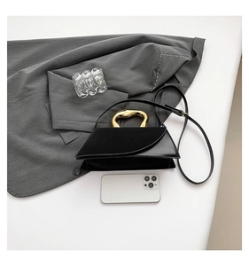 Detail of black trapezoid handbag with gold metal handle on a dark grey blazer