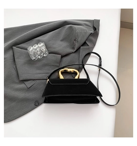 Detail of elegant black crossbody bag with unique irregular gold metal handle and gray suit