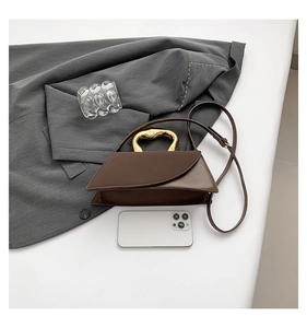 Detail of a brown trapezoid handbag with unique liquid gold metal handle and a phone for scale
