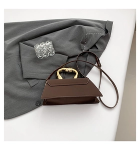 Detail of dark brown geometric handbag featuring a gold wavy handle and leather strap