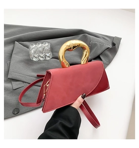 Detail of red trapezoid handbag with thick gold metal handle and matte leather texture