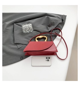 Red leather handbag with unique gold metal handle next to a white phone for size reference