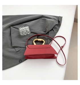 Detail of burgundy trapezoid handbag with unique wavy gold handle and matte leather finish