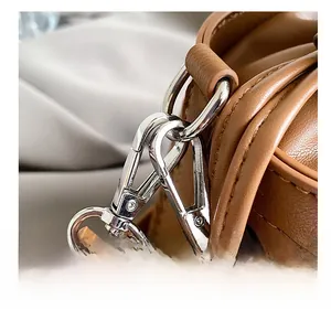 Detail of silver metal swivel hook and woven leather texture on a brown bucket bag