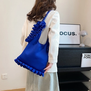 Royal blue tote bag with ruffled pleated strap design worn by model in a stylish room