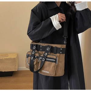 Détail du sac à bandoulière en toile marron foncé avec rivets en métal et chaînes punk