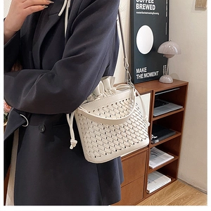 Detail of cream woven bucket bag with drawstring liner and crossbody strap on a model