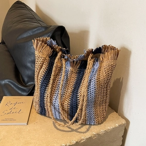 Striped straw tote bag with fringe edge and woven handles on a stone surface