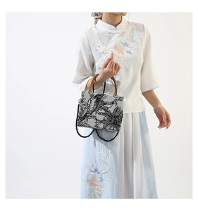 Detail view of retro bird print handbag with natural bamboo handle and beaded chain