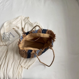 Handwoven straw tote bag with blue stripes and fringe detail for beach vacation use