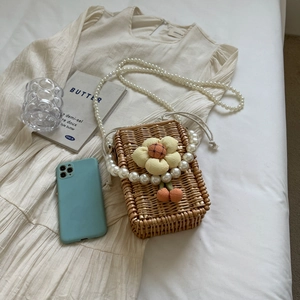 Handwoven straw crossbody bag with floral detail and pearl strap on summer dress