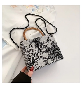 Detailed shot of embroidery forest pattern handbag with a bamboo handle and beaded chain