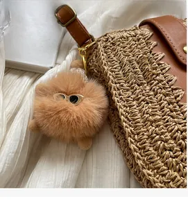 Detail of a brown fuzzy ball charm with mini sunglasses on a straw crossbody bag