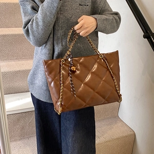 Brown quilted leather tote bag with gold chain strap carried by model in casual wear